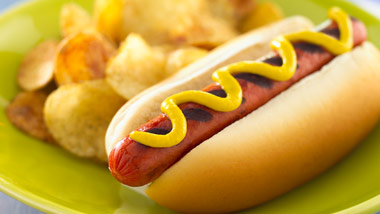 Hot dog with mustard and side of potato chips.