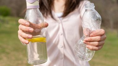 A woman holding a reusable water bottle and crushing a plastic bottle.